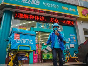 man in blue jacket and blue denim jeans standing beside green and red kanji text store