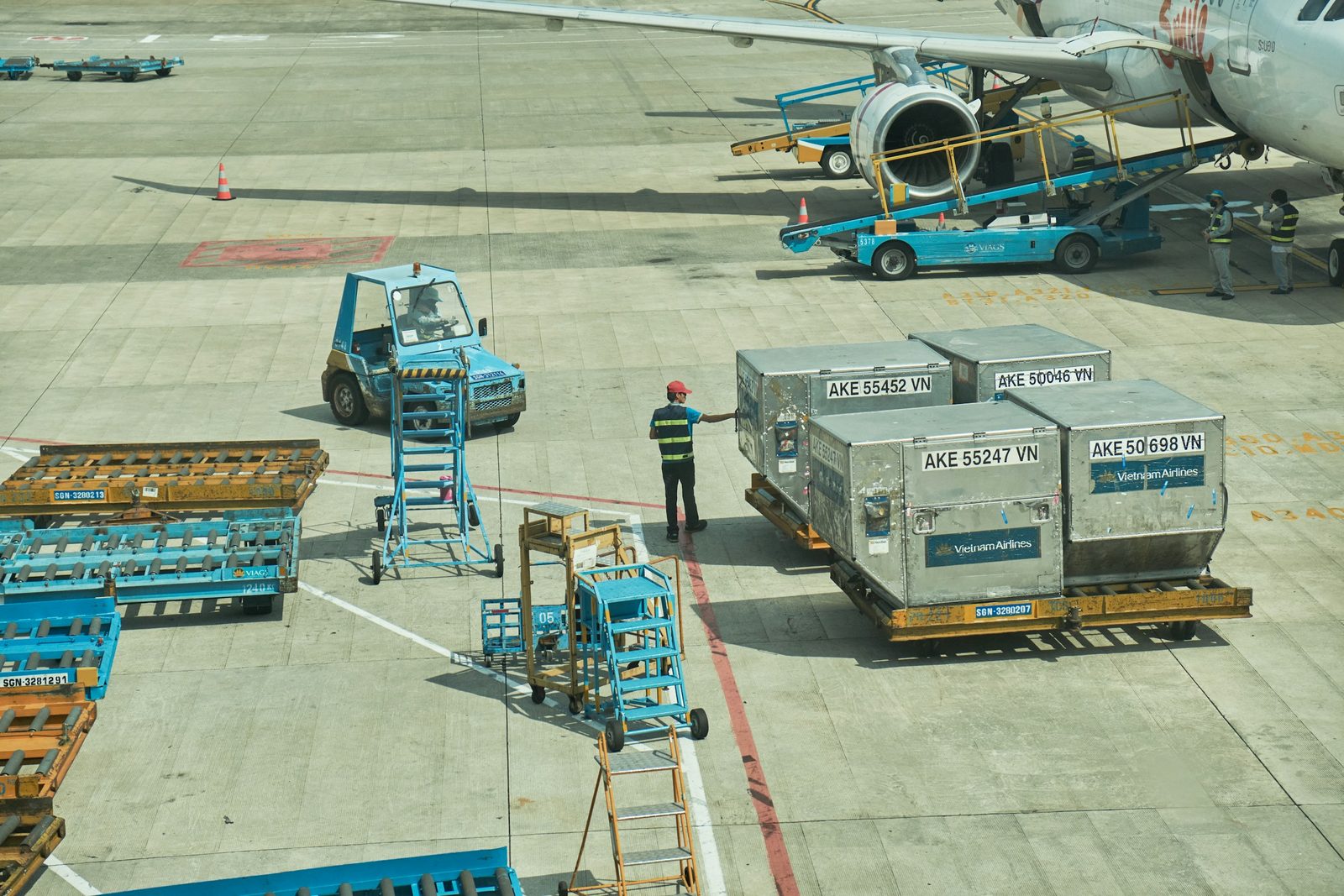 Ground crew moving air cargo ULD containers across an airport apron next to a passenger jet
