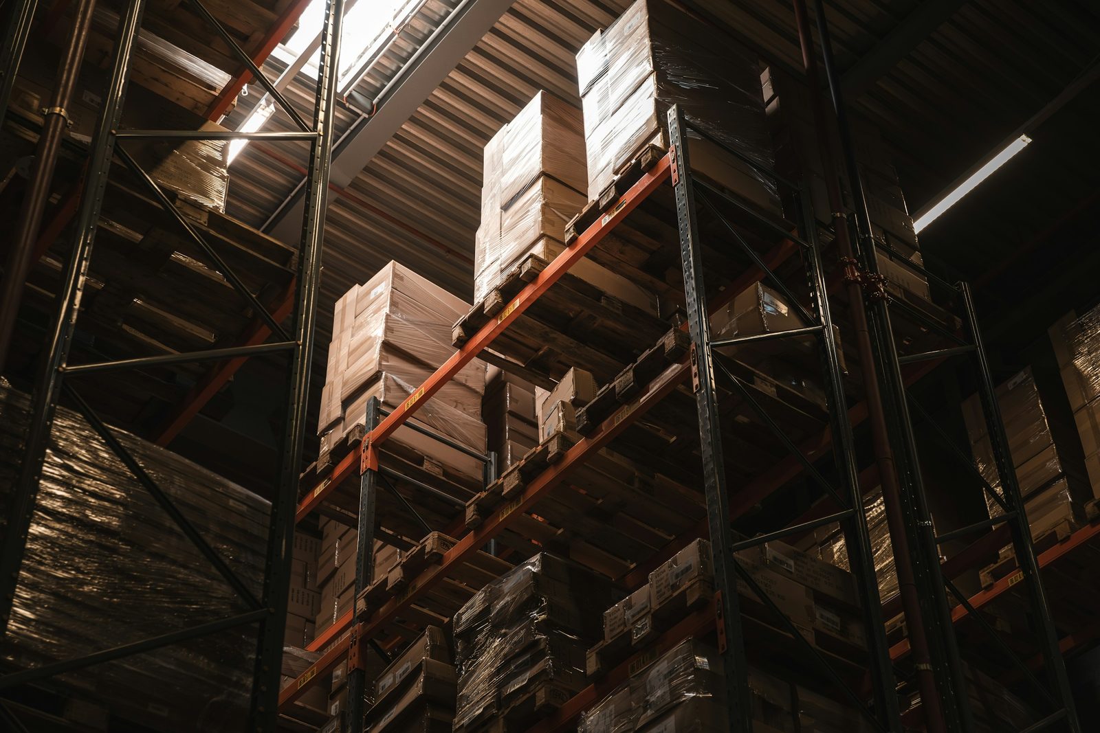 Cartons of goods stacked on tall pallet racking in a dimly lit warehouse