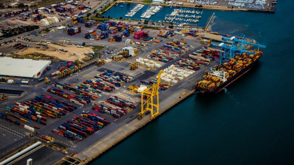 Aerial view of a container ship at berth beside ship-to-shore cranes and a busy container yard