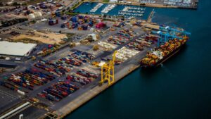 Aerial view of a container ship at berth beside ship-to-shore cranes and a busy container yard