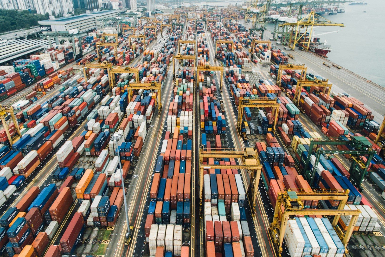 Rows of stacked shipping containers and yard gantry cranes at a large container terminal