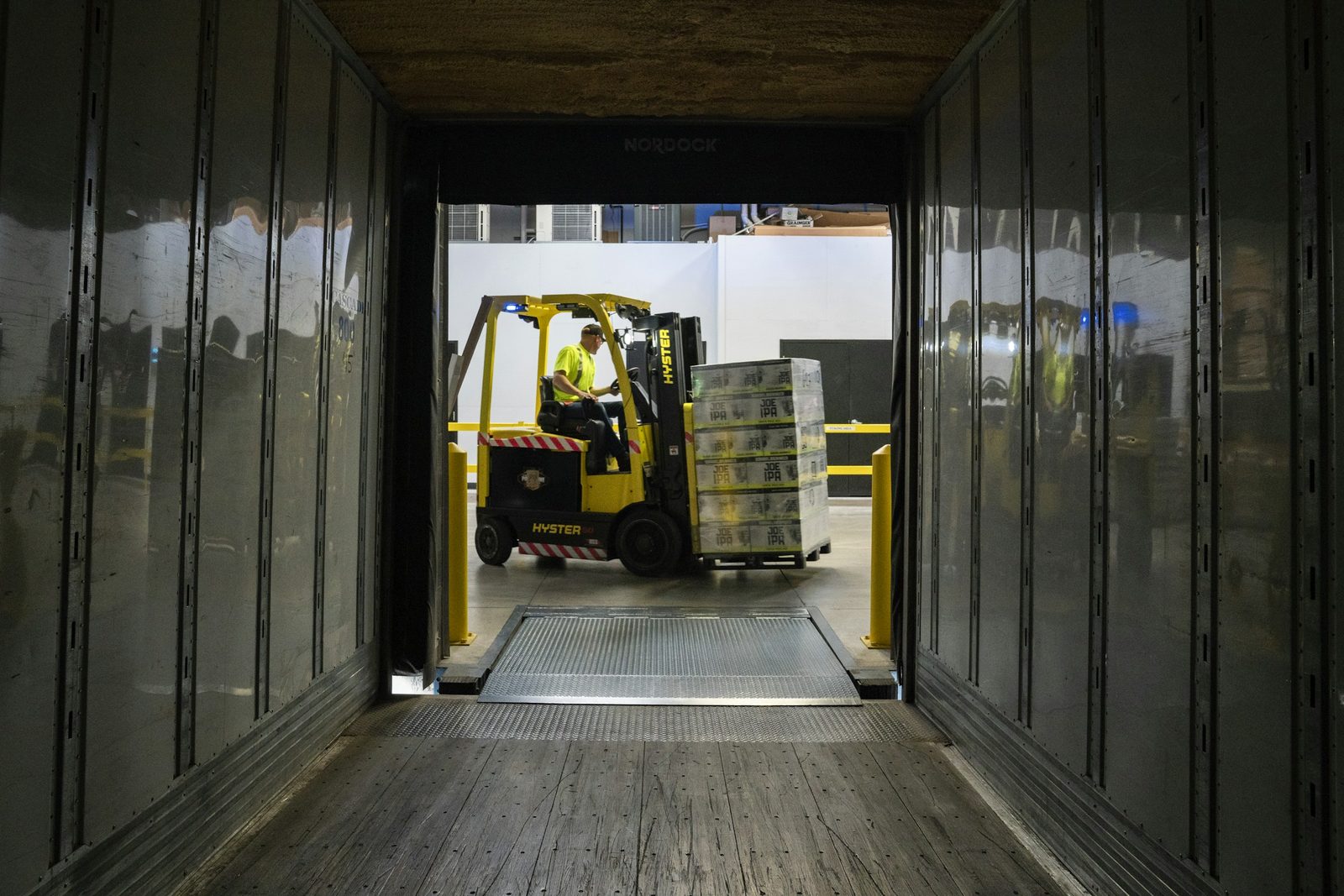 Forklift loading a wrapped pallet into a trailer, seen from inside the trailer at a loading dock