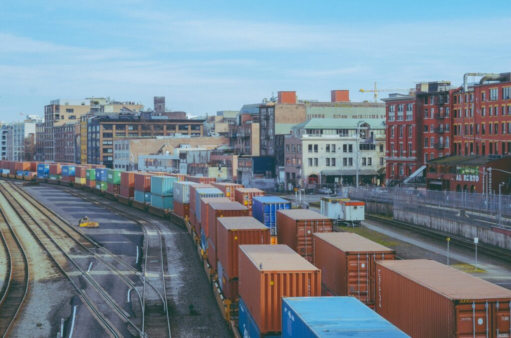Double-stack intermodal container train in a rail yard beside historic brick buildings