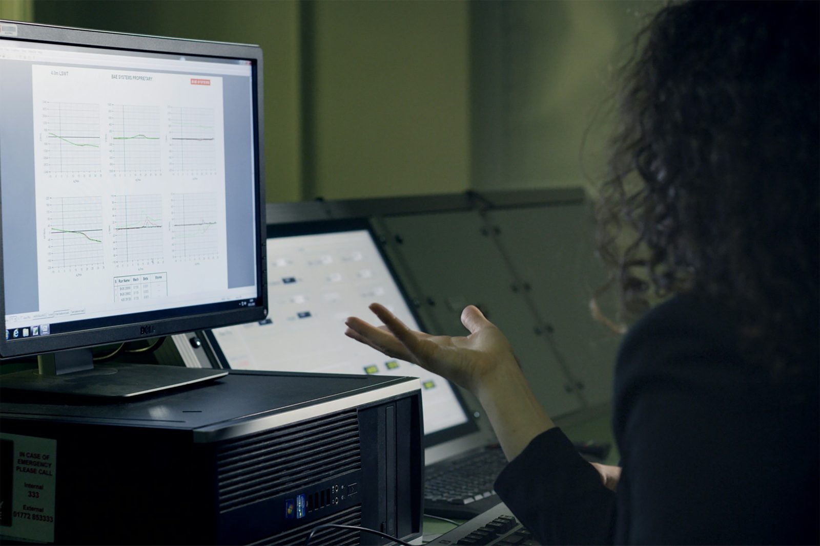 Person at a desk reviewing charts on two monitors in a dim operations office