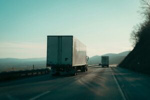 Two tractor-trailers on a divided highway through hills in early morning light