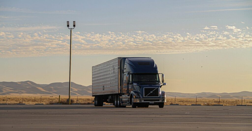 US tractor-trailer with a dry van parked on an open lot at sunrise, hills in the background